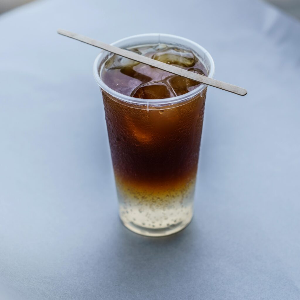 Close-up of a refreshing iced drink with gradient layers in a clear plastic cup on a neutral background.