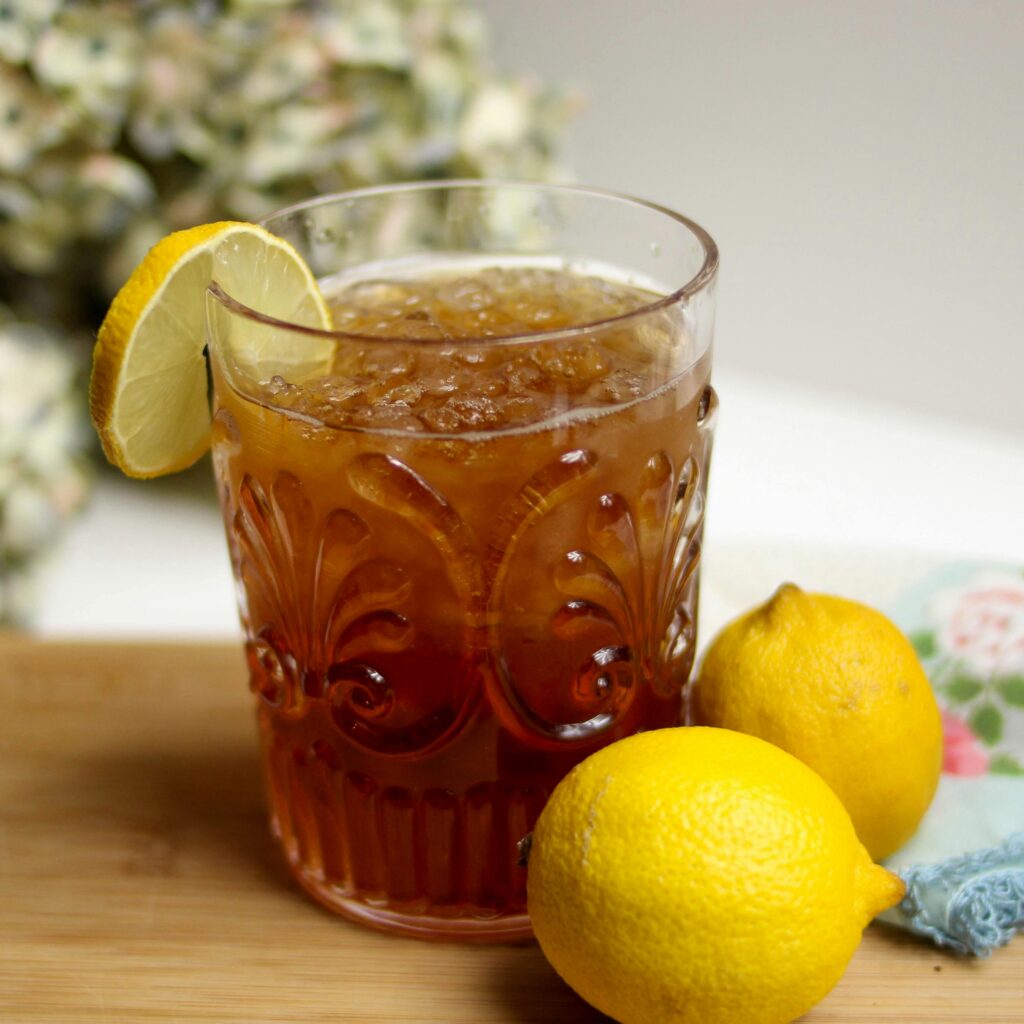 Close-up of a refreshing iced tea with lemon slices and whole lemons on a wooden table.